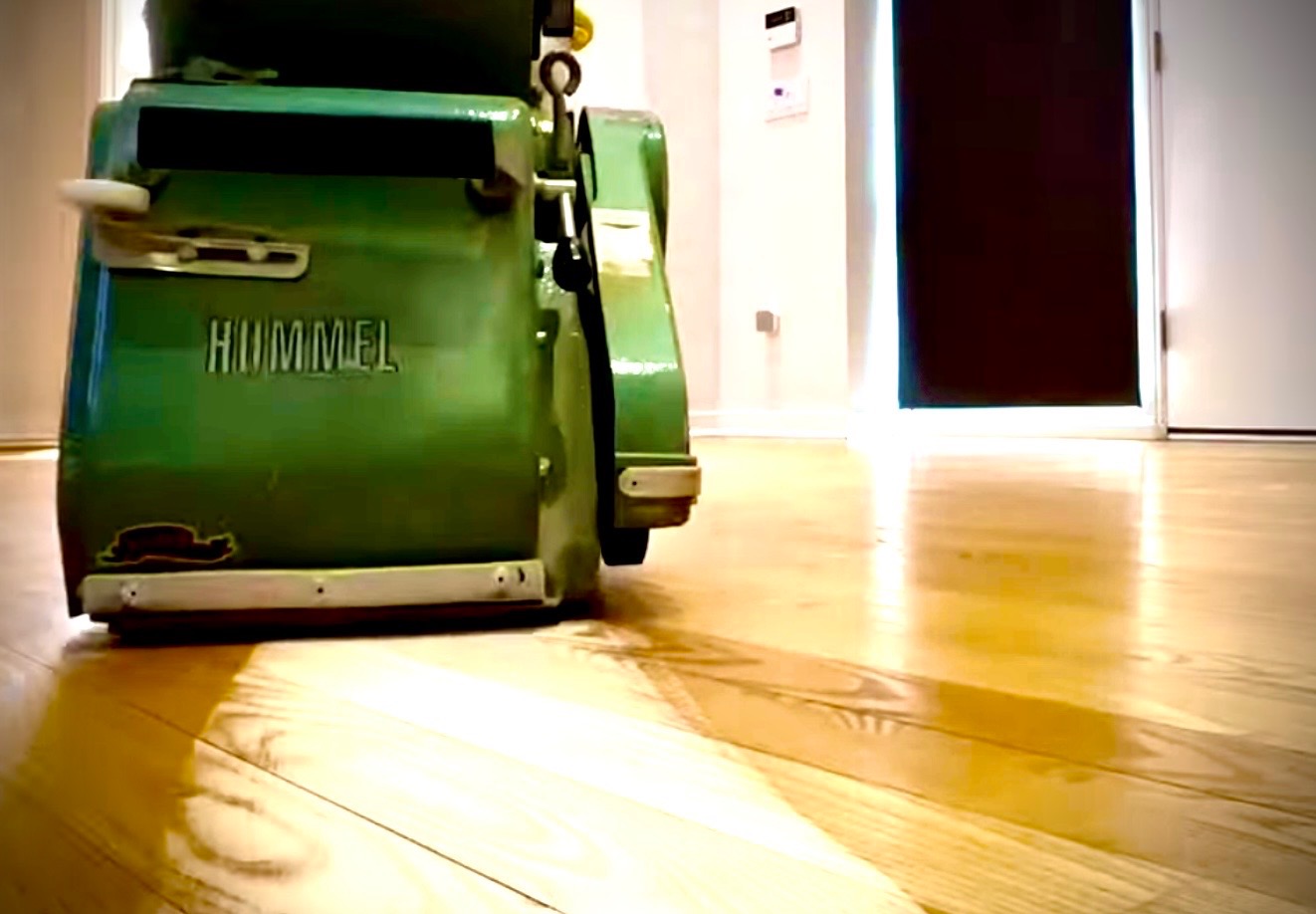 Maszyna Hummel do renowacji podłóg na błyszczącej, odnowionej drewnianej podłodze. Widoczne drzwi w tle.