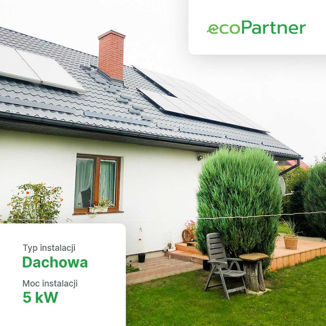Instalacja fotowoltaiczna na dachu domu jednorodzinnego z ceglanym kominem, widok z ogrodu, logo ecoPartner w prawym górnym rogu.