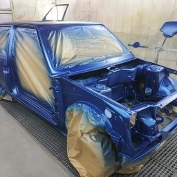 Paweł Guz PABLO-CARS - Przygotowany do lakierowania, częściowo zamaskowany folią, karoseria samochodu w odcieniach niebieskiego na ruszcie w kabinie lakierniczej, z otwartą maską.