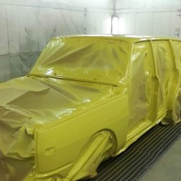 Paweł Guz PABLO-CARS - Żółty samochód osobowy, częściowo zakryty folią ochronną w lakierni, przygotowany do malowania, widoczna metalowa kratka pod pojazdem.