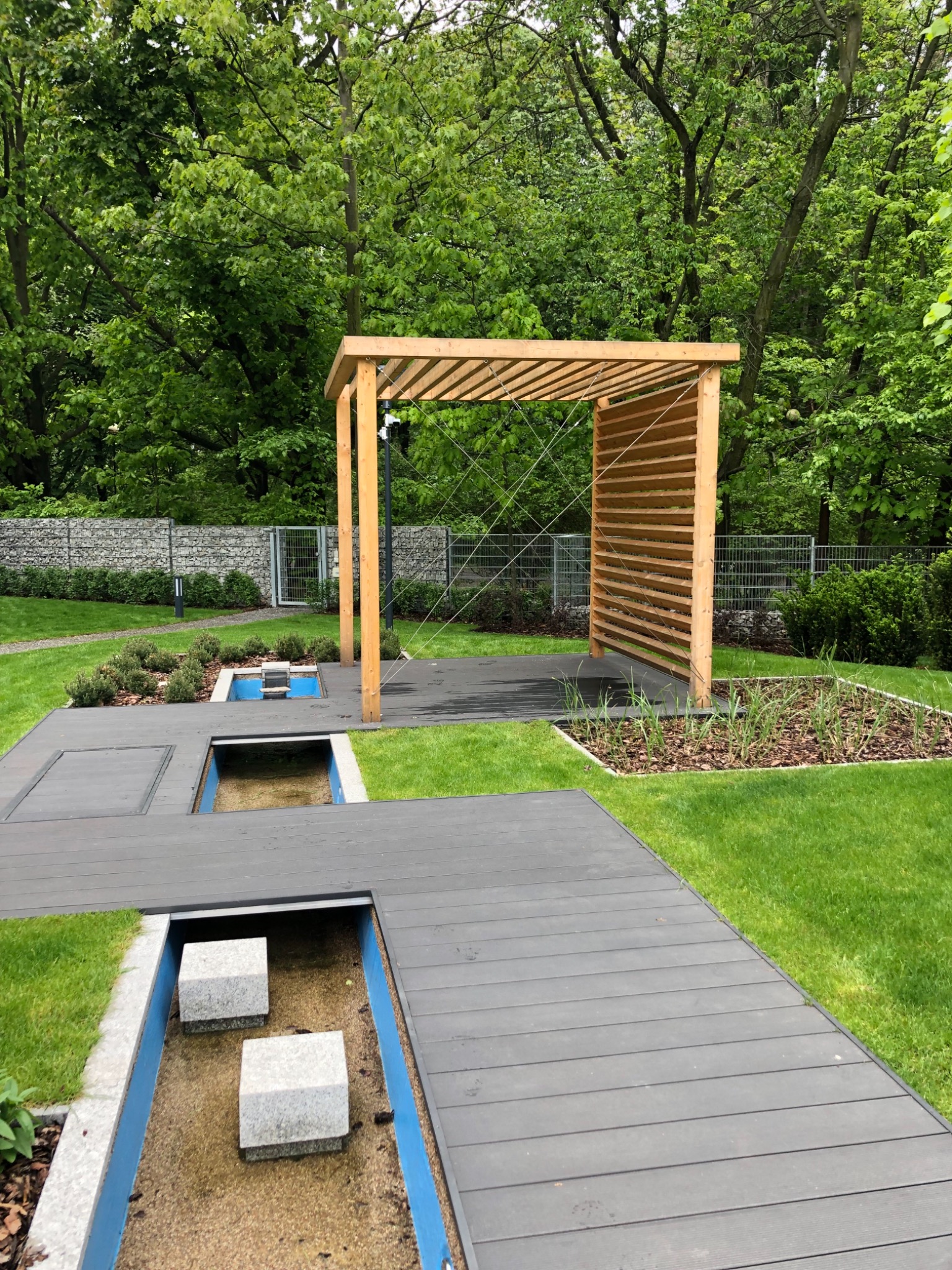 Nowoczesny ogród z drewnianą pergolą, tarasem z desek kompozytowych, elementami wodnymi i minimalistyczną architekturą krajobrazu.