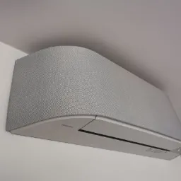 Szara klimatyzacja Toshiba zamontowana na ścianie, z obudową imitującą tkaninę, w minimalistycznym wnętrzu.