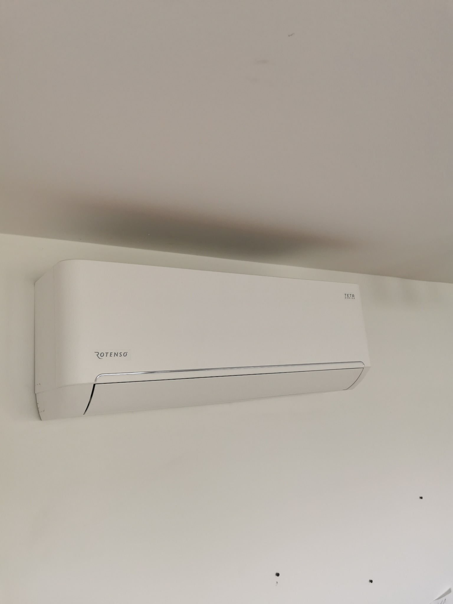 Biała jednostka wewnętrzna klimatyzacji Rotenso Teta Series zamontowana na ścianie w pomieszczeniu.