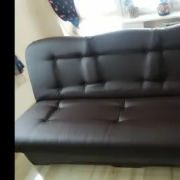 Ciemnobrązowa, skórzana sofa z guzikami, ustawiona w pokoju z widokiem na okno z roślinami.