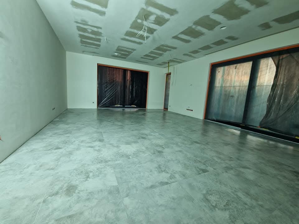 Wykończone płytki podłogowe w przestronnym pokoju z przygotowanym sufitem podwieszanym i zabezpieczonymi folią oknami, gotowym do dalszych prac wykończeniowych.