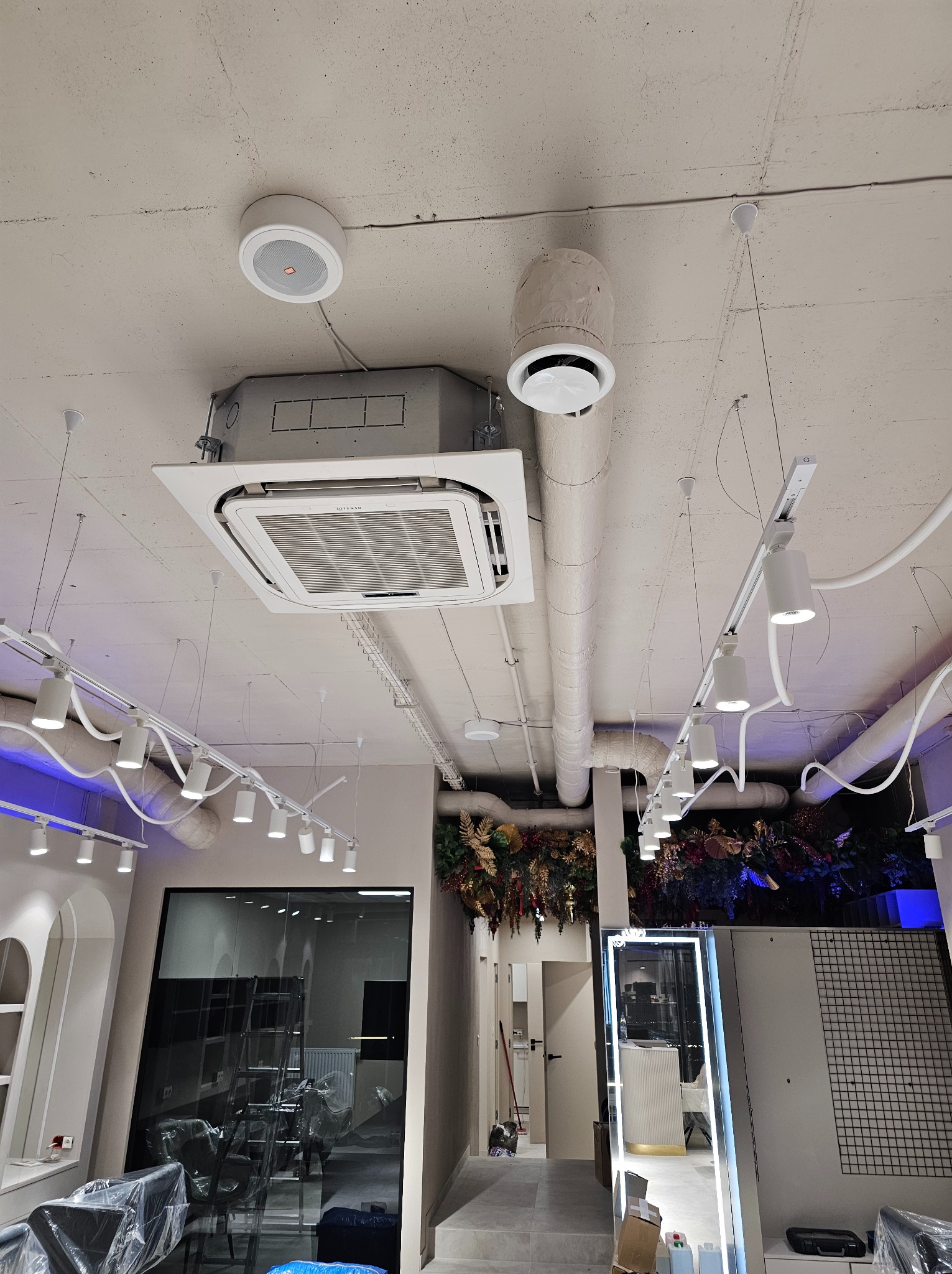 Sufit w lokalu komercyjnym z zainstalowaną kasetonową jednostką klimatyzacyjną, okrągłym nawiewnikiem i oświetleniem szynowym.