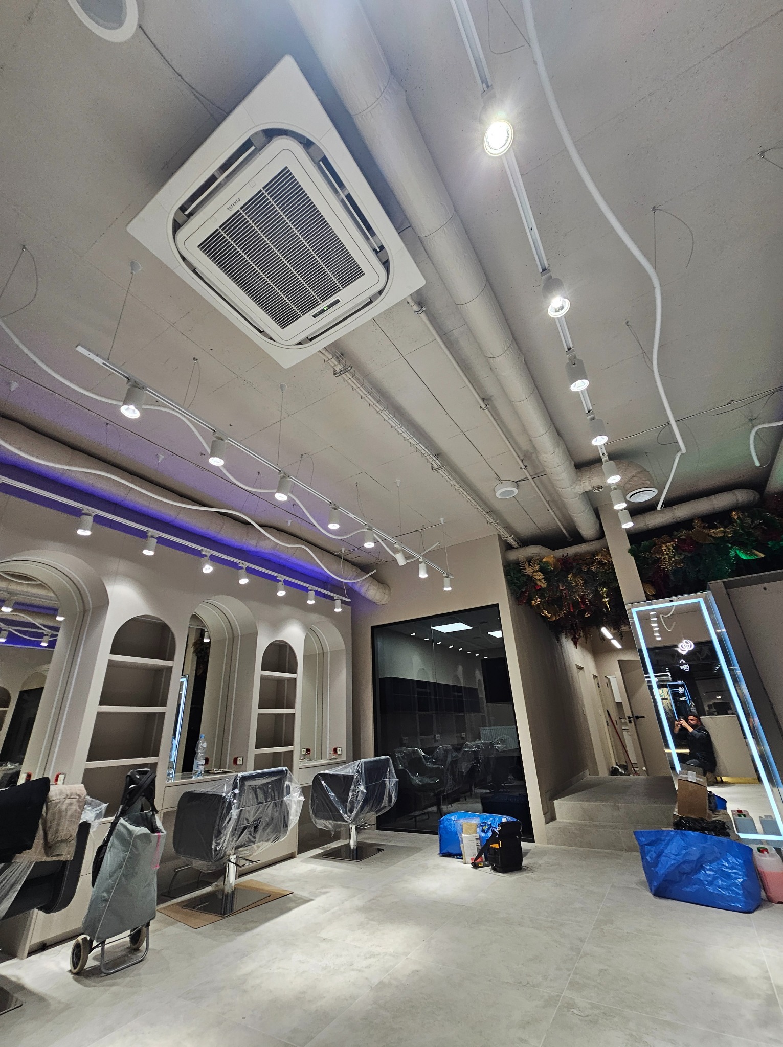 Klimatyzacja kasetonowa zamontowana w salonie fryzjerskim w Warszawie, widoczne instalacje oświetleniowe i stanowiska pracy w trakcie przygotowywania.