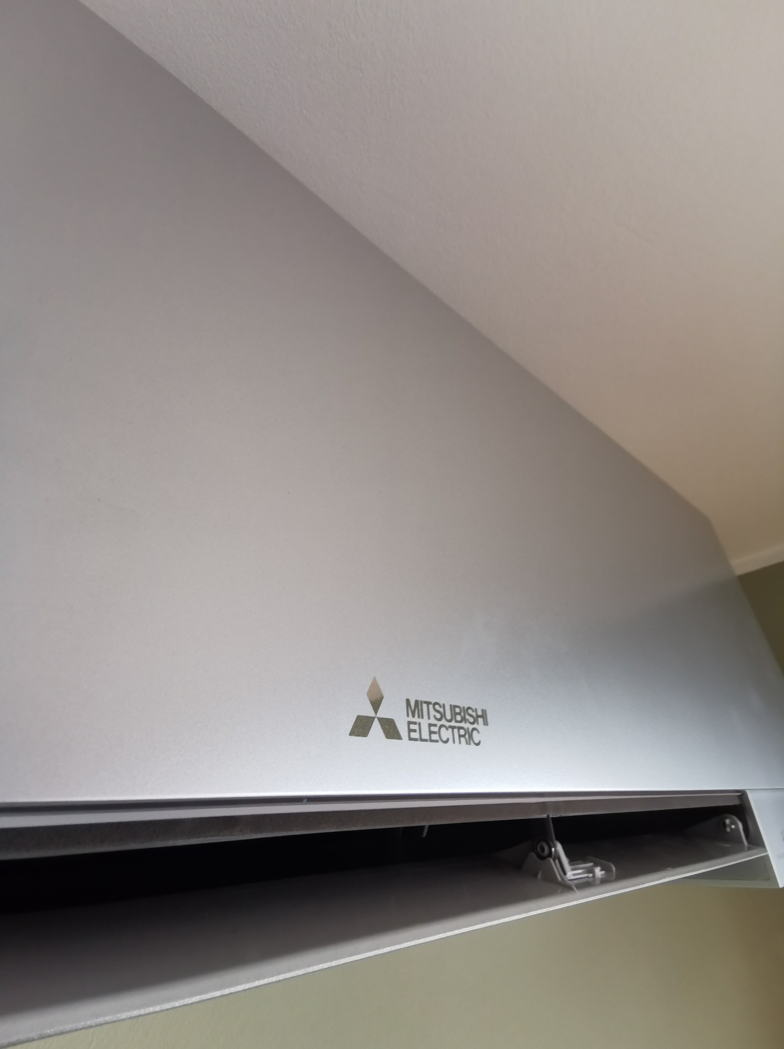 Zamontowany klimatyzator Mitsubishi Electric na ścianie, widoczne logo i otwarty wylot powietrza.