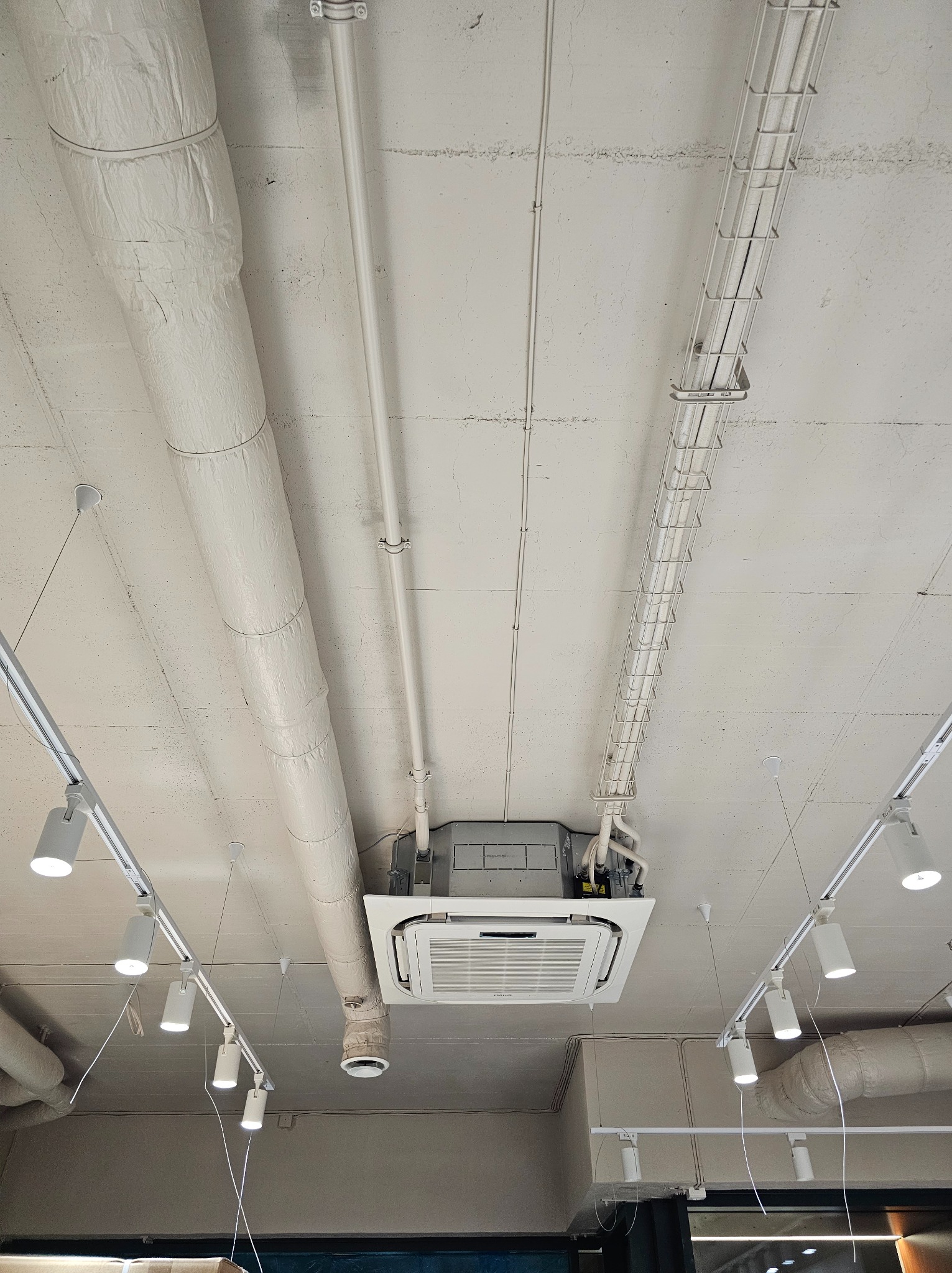 Kasetonowa klimatyzacja sufitowa z widocznymi instalacjami wentylacyjnymi i oświetleniem punktowym w pomieszczeniu biurowym.