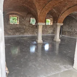 Świeżo wylana, gładka posadzka w zabytkowym pomieszczeniu z ceglanym sklepieniem łukowym i kamiennymi filarami, widoczne ślady po butach.