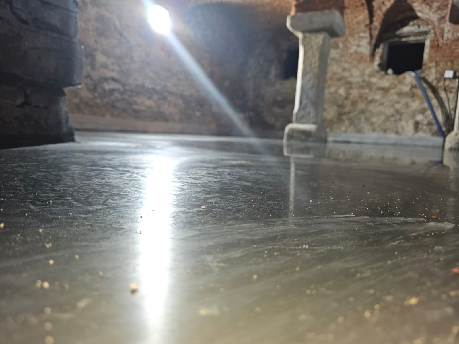 Świeżo wylana, błyszcząca posadzka przemysłowa w piwnicy ze sklepieniem łukowym, z widocznymi kamiennymi filarami i śladami po narzędziach.