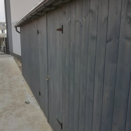 ROBUD - Szare drewniane ogrodzenie z metalowymi zawiasami, widok z boku, z rynną wzdłuż górnej krawędzi, obok wyłożona płytami ścieżka.