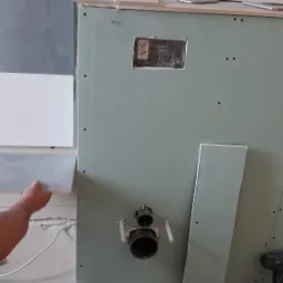 Przymiarka szarej płytki do ściany z zamontowaną instalacją wodną i płytami kartonowo-gipsowymi, widoczne otwory na półki i narzędzia