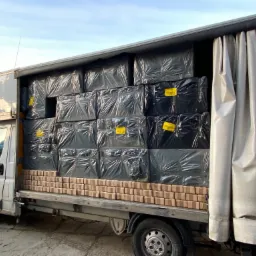 Bus transportuje palety cegieł i zapakowane w folię towary z żółtymi etykietami w przestrzeni ładunkowej z częściowo odsłoniętą plandeką.