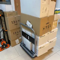 Dwa wózki transportowe załadowane kartonami różnej wielkości, gotowe do przewiezienia w biurze.