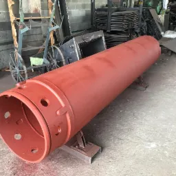 Czerwony, pomalowany walec metalowy z otworami, umieszczony na metalowych wspornikach w warsztacie.