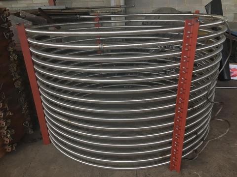 Spiralna rura ze stali nierdzewnej, podparta czerwonymi profilami, widoczna w warsztacie.