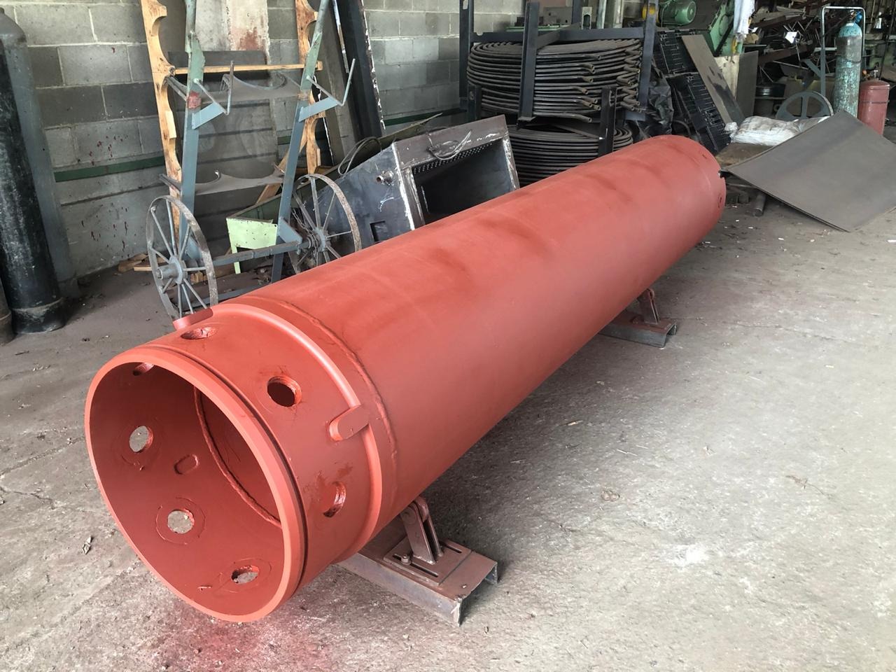 Czerwony, pomalowany walec metalowy z otworami, umieszczony na metalowych wspornikach w warsztacie.