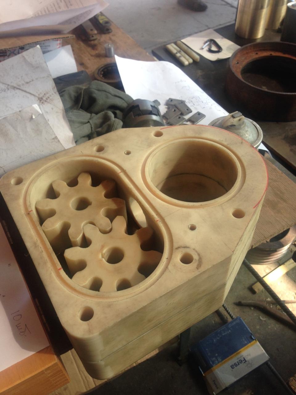 Beżowy blok z tworzywa sztucznego z wyfrezowanymi dwoma komorami, w jednej z nich umieszczone dwa koła zębate. W tle widoczne narzędzia i notatki.