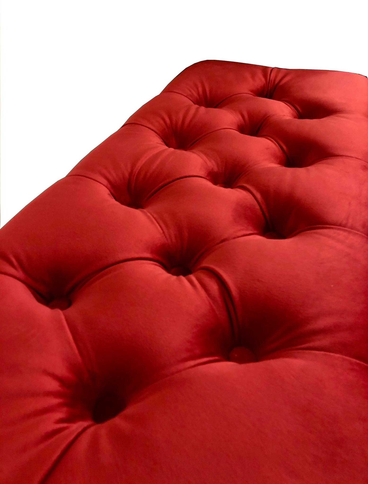 Fragment czerwonego, tapicerowanego pufa z głębokimi pikowaniami w stylu chesterfield.