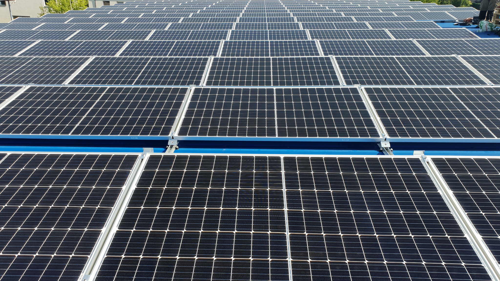 Instalacja fotowoltaiczna 40kWp w Łomży: widok z góry na rząd paneli słonecznych na niebieskim dachu, widoczne metalowe mocowania.