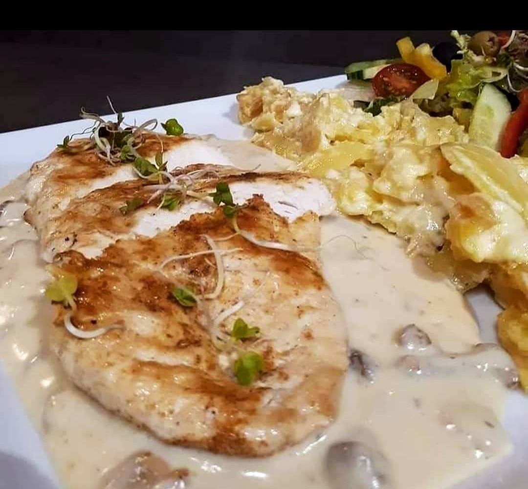 Grillowana pierś z kurczaka w sosie grzybowym, podana z sałatką i ziemniakami z sosem, na białym talerzu.