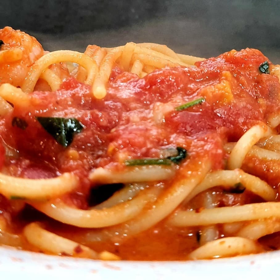 Parujące spaghetti z gęstym sosem pomidorowym i bazylią, podane na białym talerzu.