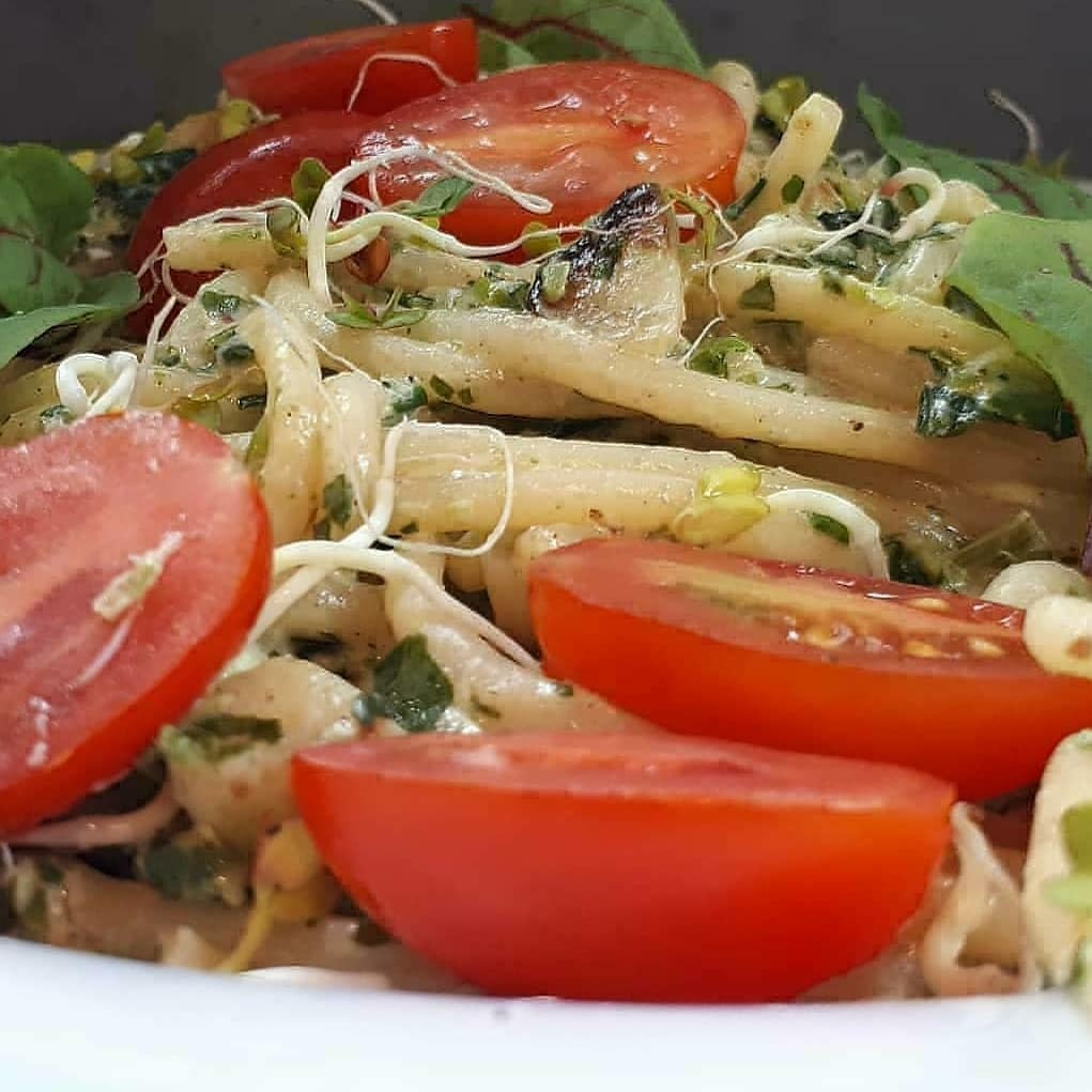 Makaron w kremowym sosie z ziołami, udekorowany połówkami pomidorów i kiełkami, prezentowany z bliska.