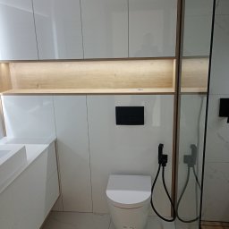 Expert wykończenia wnętrz - Nowoczesna łazienka z białymi, lakierowanymi szafkami, podświetlaną półką i toaletą z bidetką. Marmurowe płytki podłogowe. Minimalistyczny design.