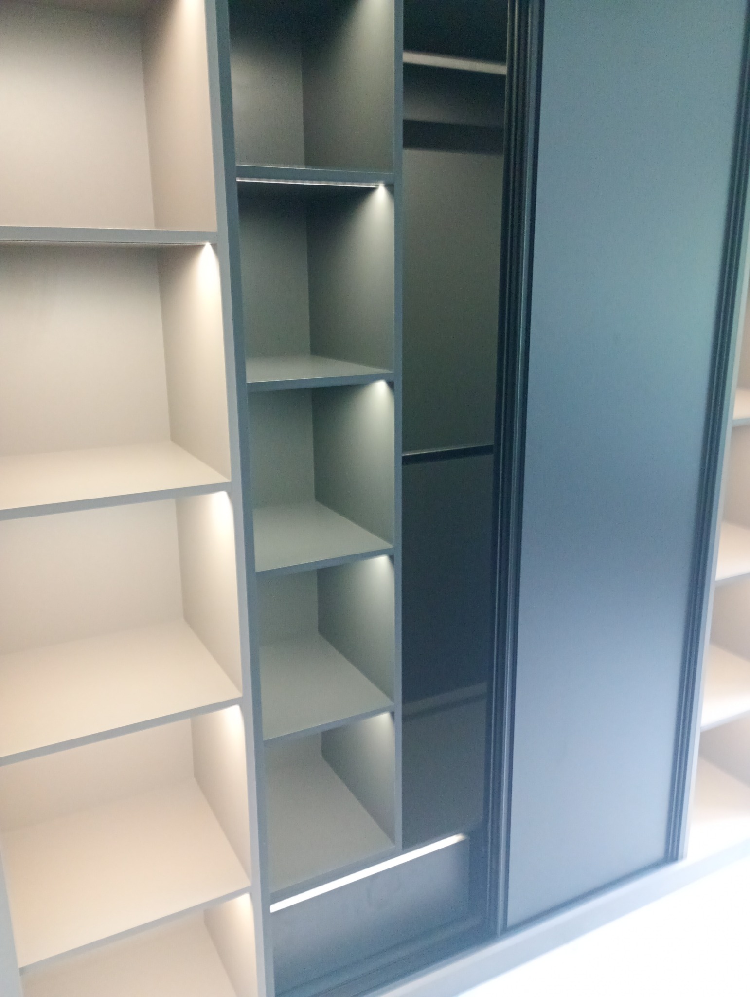 Nowoczesna szafa wnękowa z przesuwnymi drzwiami w odcieniach szarości i beżu, oświetlona punktowo, prezentująca puste półki i minimalistyczny design.