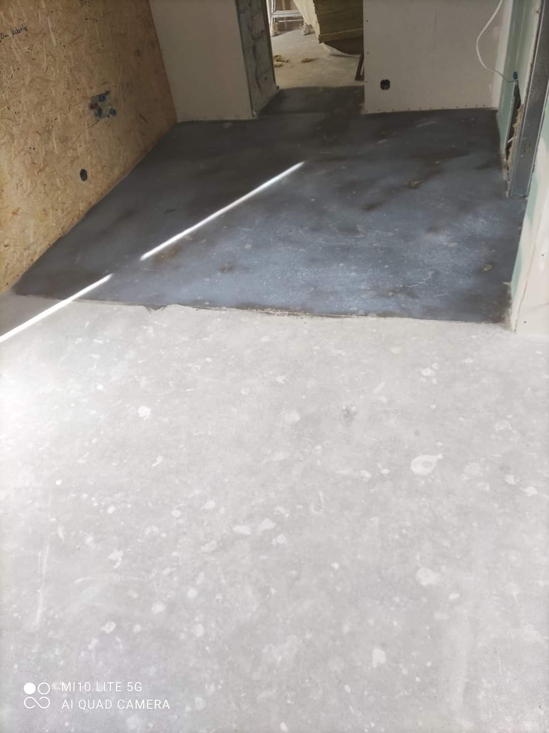 Wyrównana podłoga w trakcie remontu, widoczne dwie warstwy wylewki, ściany w surowym stanie, fragment płyty OSB na ścianie.