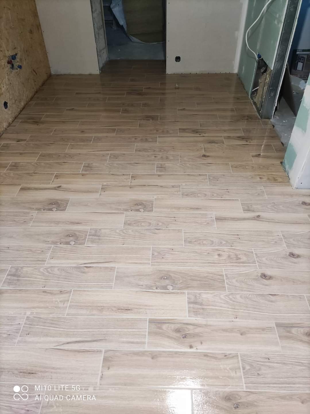 Ułożone podłużne płytki podłogowe imitujące drewno w surowym wnętrzu, widoczne przygotowane ściany do dalszych prac.