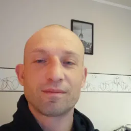 Portret mężczyzny w bluzie z kapturem, na ścianie widoczny obrazek z wieżą i tapeta z motywem tulipanów.