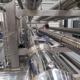 Spaw System Weldnig Group - Instalacja przemysłowa z rurami ze stali nierdzewnej w Warszawie, pracownik w okularach reguluje rurę z karbowaną powierzchnią.