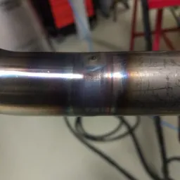 Poziome ujęcie spoiny na metalowej rurze, widoczne ślady termiczne i przebarwienia po procesie łączenia.