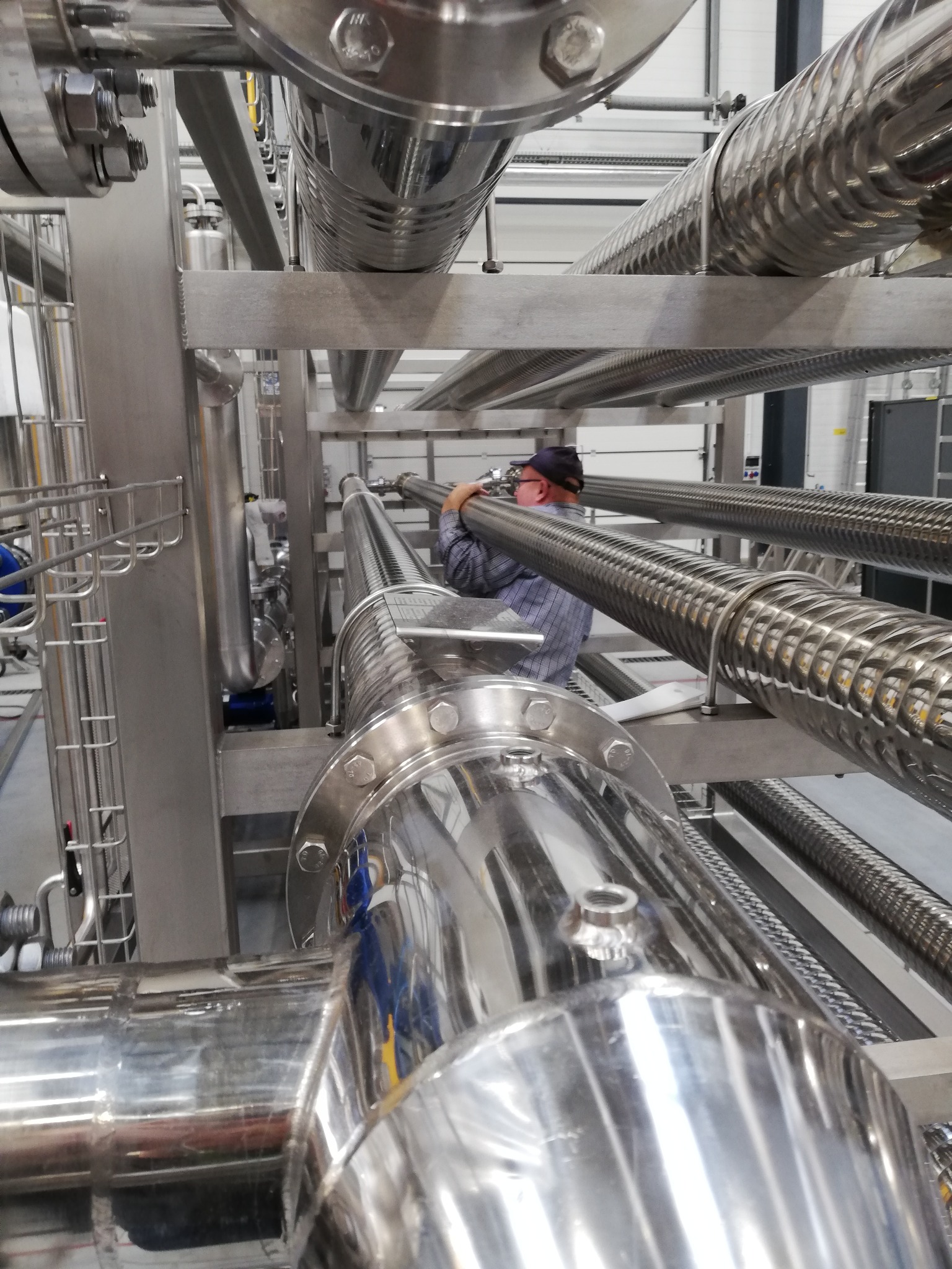 Instalacja przemysłowa z rurami ze stali nierdzewnej w Warszawie, pracownik w okularach reguluje rurę z karbowaną powierzchnią.