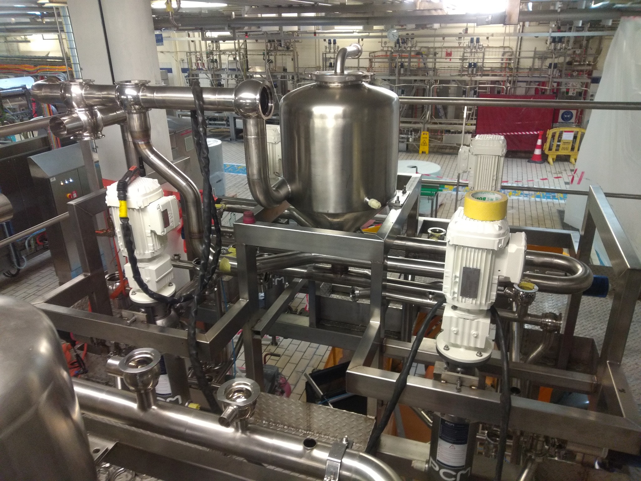Kompleksowa instalacja przemysłowa ze stali nierdzewnej, z widocznymi silnikami elektrycznymi, zbiornikiem ciśnieniowym i licznymi rurami oraz zaworami w hali produkcyjnej.