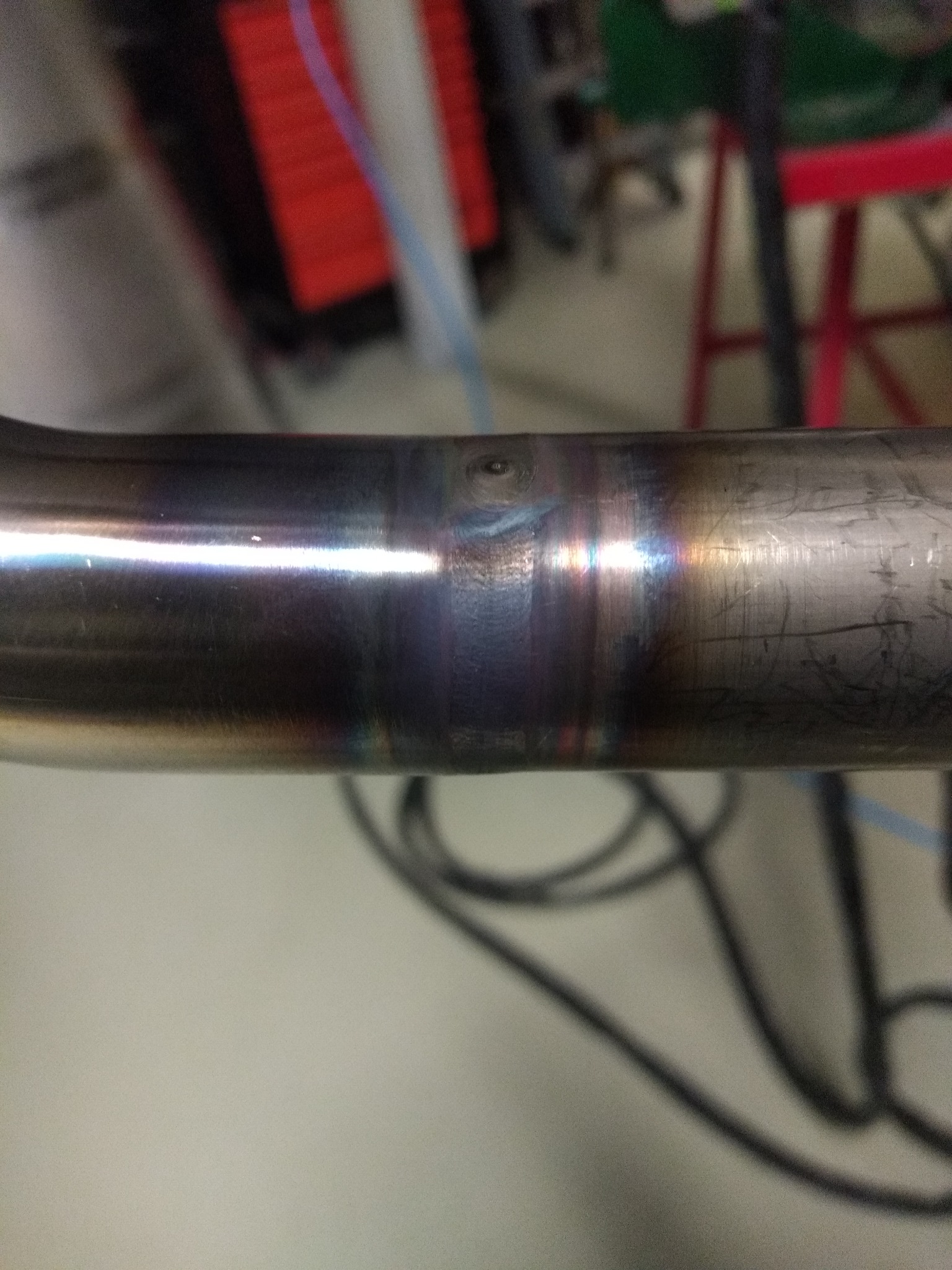 Poziome ujęcie spoiny na metalowej rurze, widoczne ślady termiczne i przebarwienia po procesie łączenia.