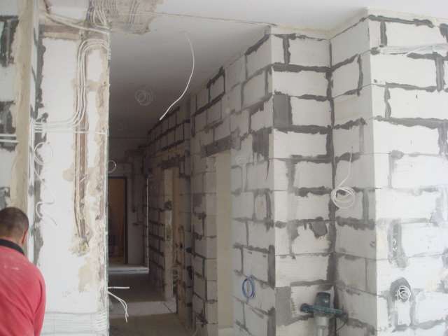 Wnętrze w trakcie przebudowy: ściany z białych bloczków betonowych, widoczne instalacje elektryczne, surowy stan wykończenia.
