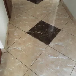 Beżowa podłoga z marmurowym wzorem ułożona z kwadratowych płytek z ciemnobrązowymi akcentami w romby, widok z góry na korytarz.