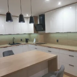 Nowoczesna kuchnia z białymi szafkami, drewnianym blatem i wyspą, oświetlona trzema czarnymi lampami wiszącymi. W tle czarny okap i lodówka z magnesami.