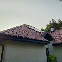 Panele słoneczne na brązowym dachu domu jednorodzinnego z anteną satelitarną i anteną radiową, widok z dołu.