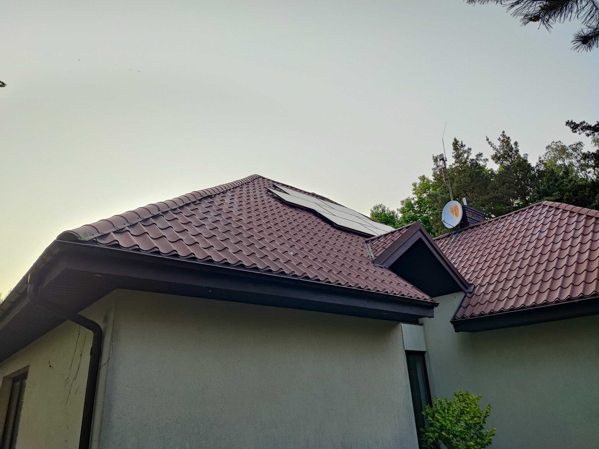 Panele słoneczne na brązowym dachu domu jednorodzinnego z anteną satelitarną i anteną radiową, widok z dołu.