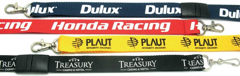 Cztery kolorowe smycze reklamowe z różnymi nadrukami firmowymi: Dulux (granatowa), Honda Racing (czerwona), Plaut (żółta) i Treasury Casino & Hotel (czarna), każda zakończona metalowym karabińczykiem.