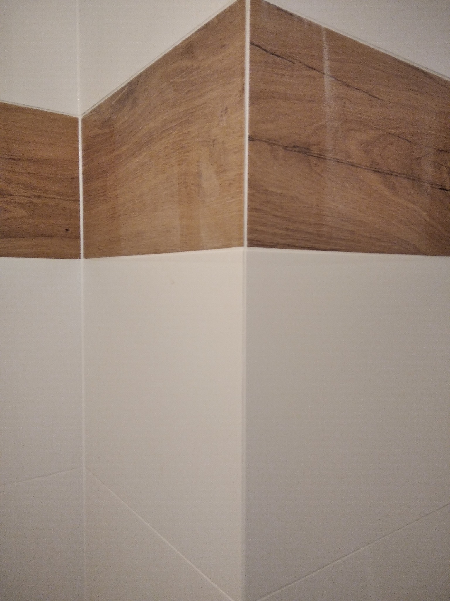 Połączenie białych i drewnopodobnych płytek w rogu pomieszczenia, widoczne fugi i dokładne wykończenie.