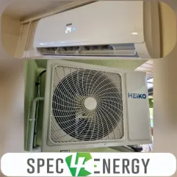 Zestaw klimatyzacji HEIKO: jednostka wewnętrzna z wyświetlaczem 24 stopnie Celsjusza i jednostka zewnętrzna zamontowana na zielonej ścianie z widocznymi rurami instalacyjnymi, z logo firmy...