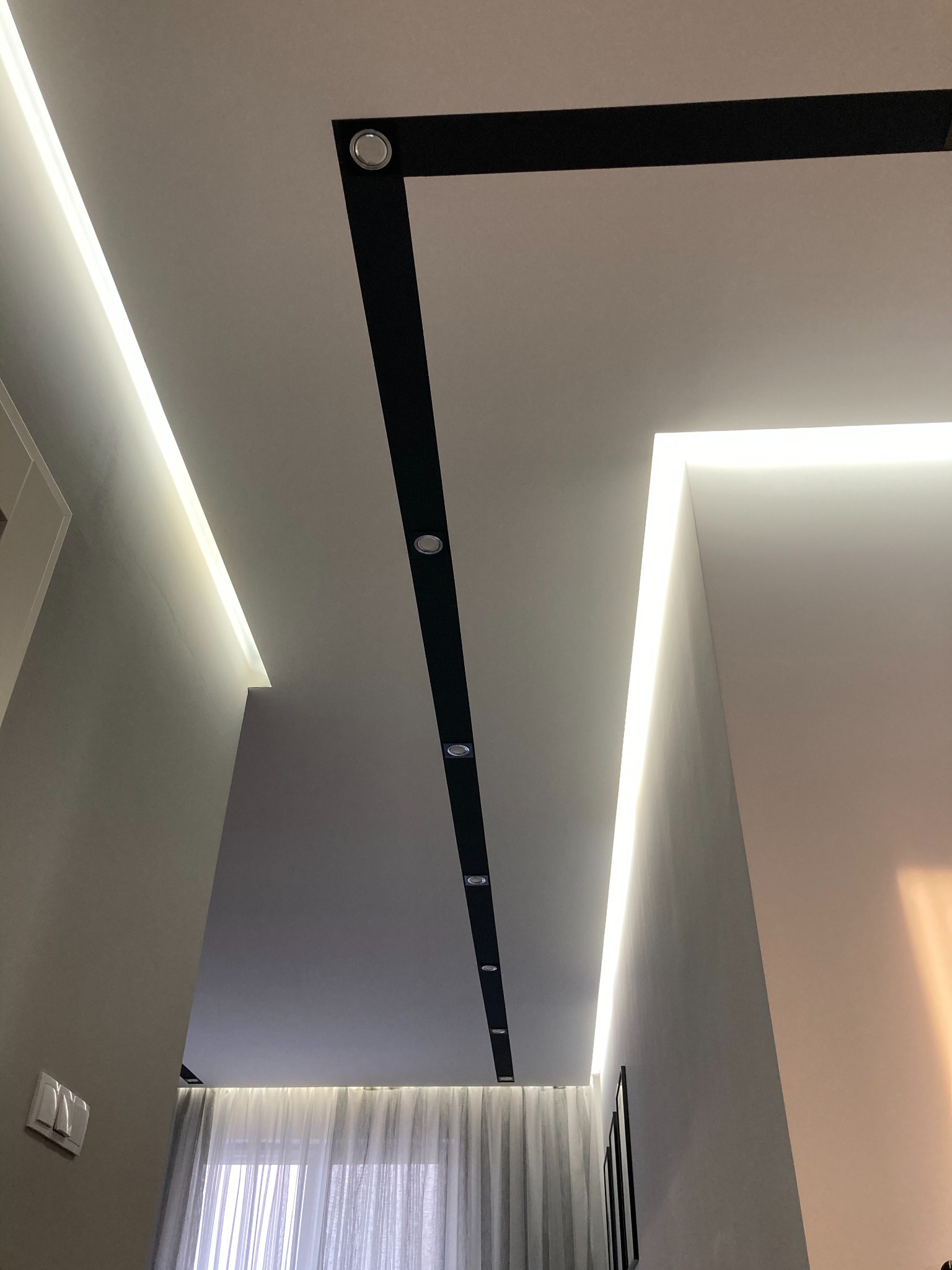 Nowoczesny sufit z podwieszanymi elementami w kolorze czarnym, oświetleniem LED wzdłuż krawędzi i punktowymi lampami, widok z dołu.