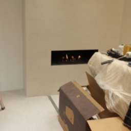 AMIGOS USŁUGI BUDOWLANO REMONTOWE TOMASZ ŹRÓDŁOWSKI - Ściana po nałożeniu gładzi, z wbudowanym kominkiem elektrycznym, narzędzia malarskie pod folią ochronną i rozpakowane opakowanie produktu na podłodze.