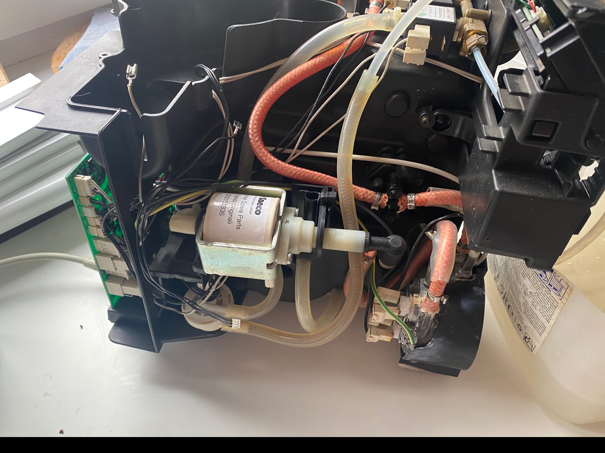 Wnętrze ekspresu do kawy z widocznymi przewodami, pompą i elementami elektroniki, na białym tle.