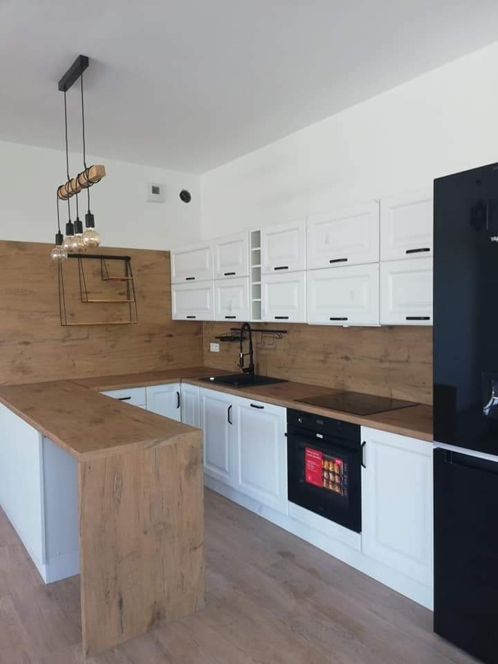 Nowoczesna kuchnia z białymi szafkami, drewnianym blatem i panelem ściennym, czarną armaturą i oświetleniem w stylu loft.